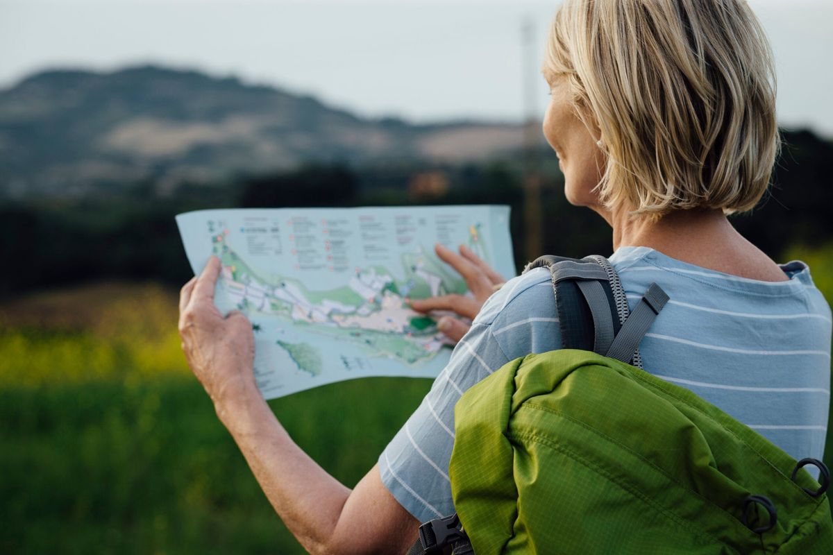 Person with a green backpack reading a map outdoors in nature.
